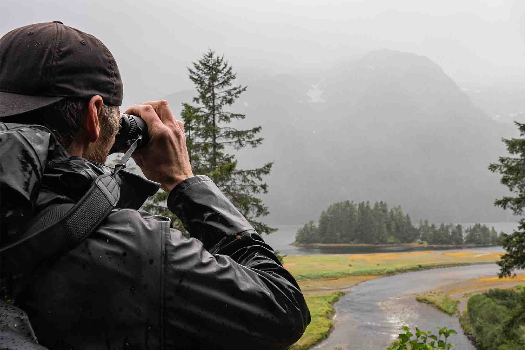 man birding and looking towards foggy mountains with binoculars