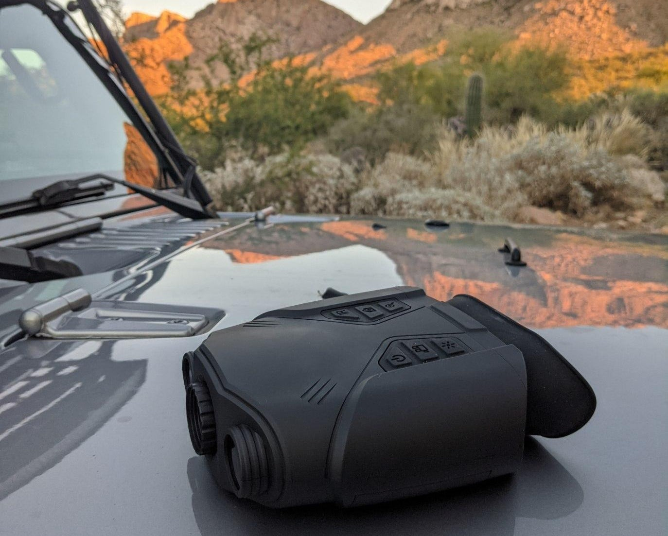 Night vision binoculars sitting on the hood of a vehicle